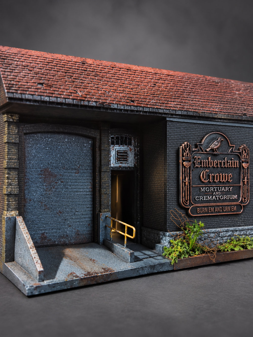 A miniature diorama model of a gothic-style crematorium building, featuring a dark gray brick facade, a rusted red-tiled roof, a closed metal garage door, and a bronze sign reading 'Emberclain Crowe Mortuary Crematorium'.